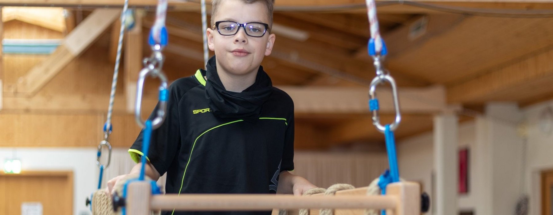 Junge steht in einem Halben Holz käfig welcher von Vier Seilen getragen wird.