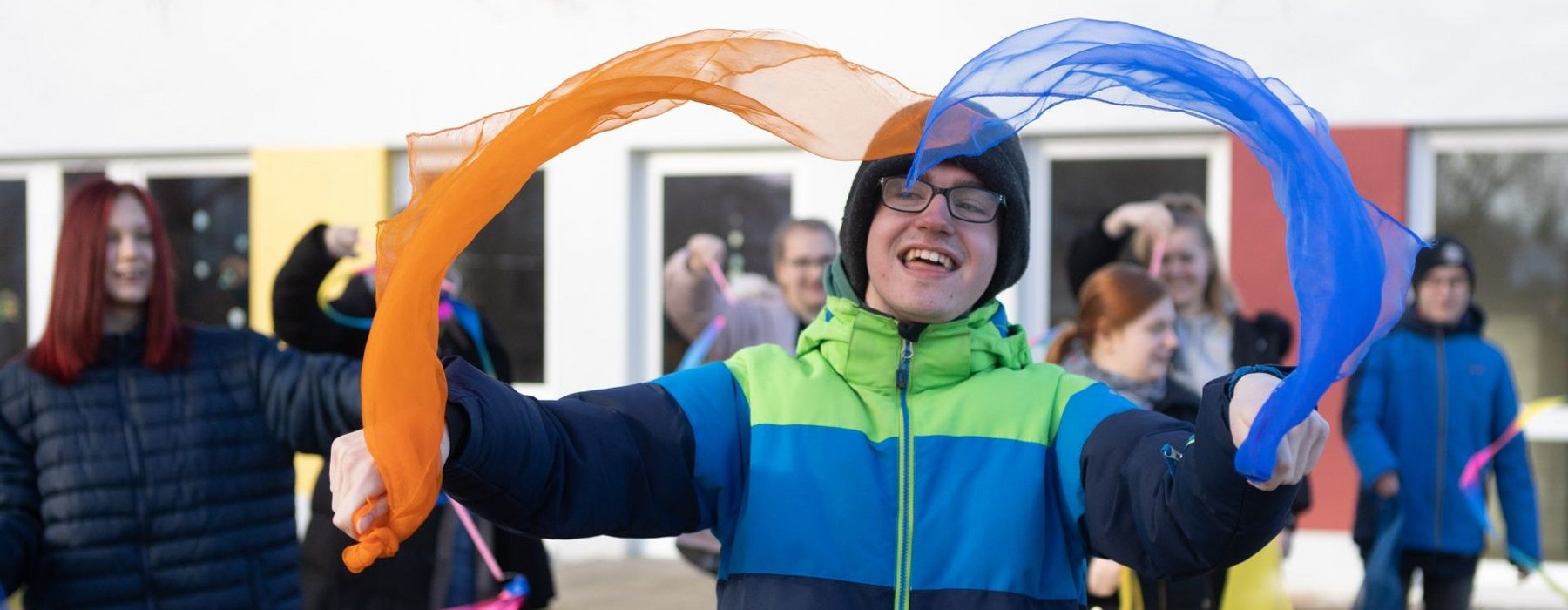Ein Junge Spielt mit Farbigen Tüchern hinter ihm sind noch mehr Kinder die mit Tüchern spielen