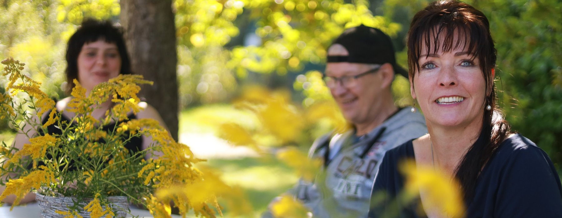 Eine Frau schaut Nett in die Kamera, im Hintergrund sind zwei andere Personen zu sehen.